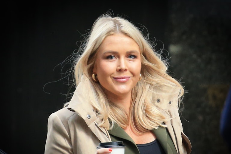 Karoline Leavitt smiles and holds a coffee while walking out of Trump Tower