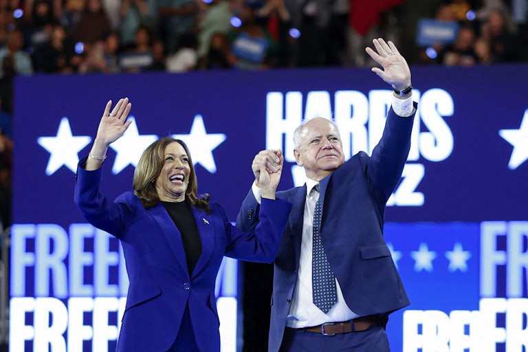 Kamala Harris and Tim Walz hold hands and wave to the crowd at a campaign rally.