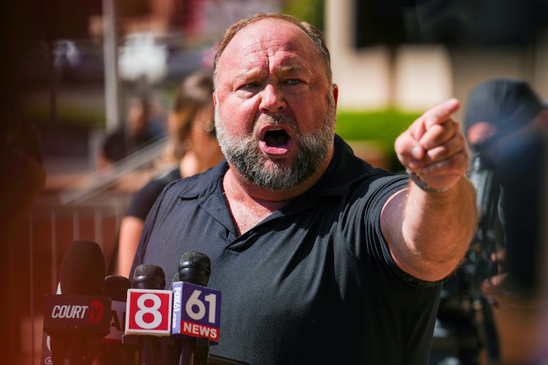Alex Jones points while speaking into news outlet microphones
