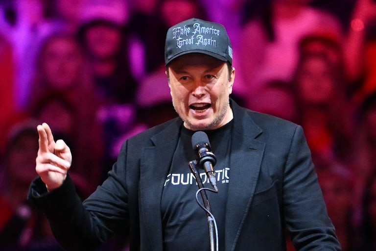 Elon Musk speaks at a Donald Trump campaign rally while wearing a black MAGA cap