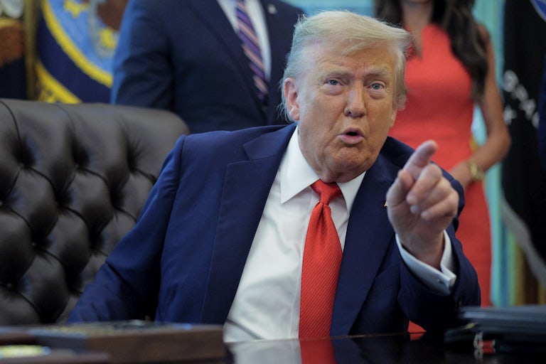 Donald Trump speaks and points at the camera while sitting at his desk in the Oval Office of the White House.