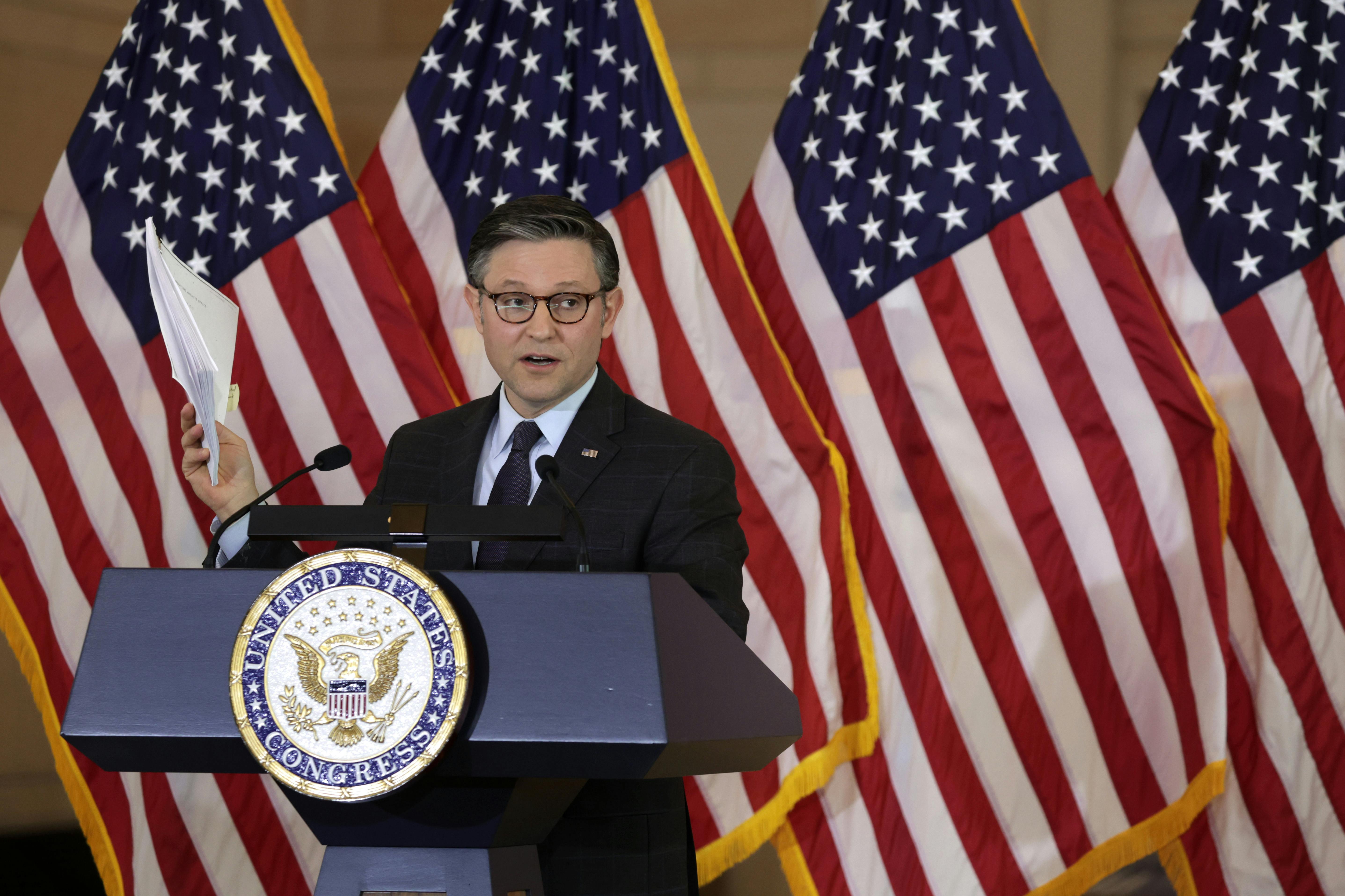 Mike Johnson stands at a podium in front of American flags.