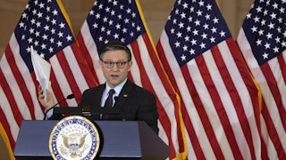Mike Johnson stands at a podium in front of American flags.