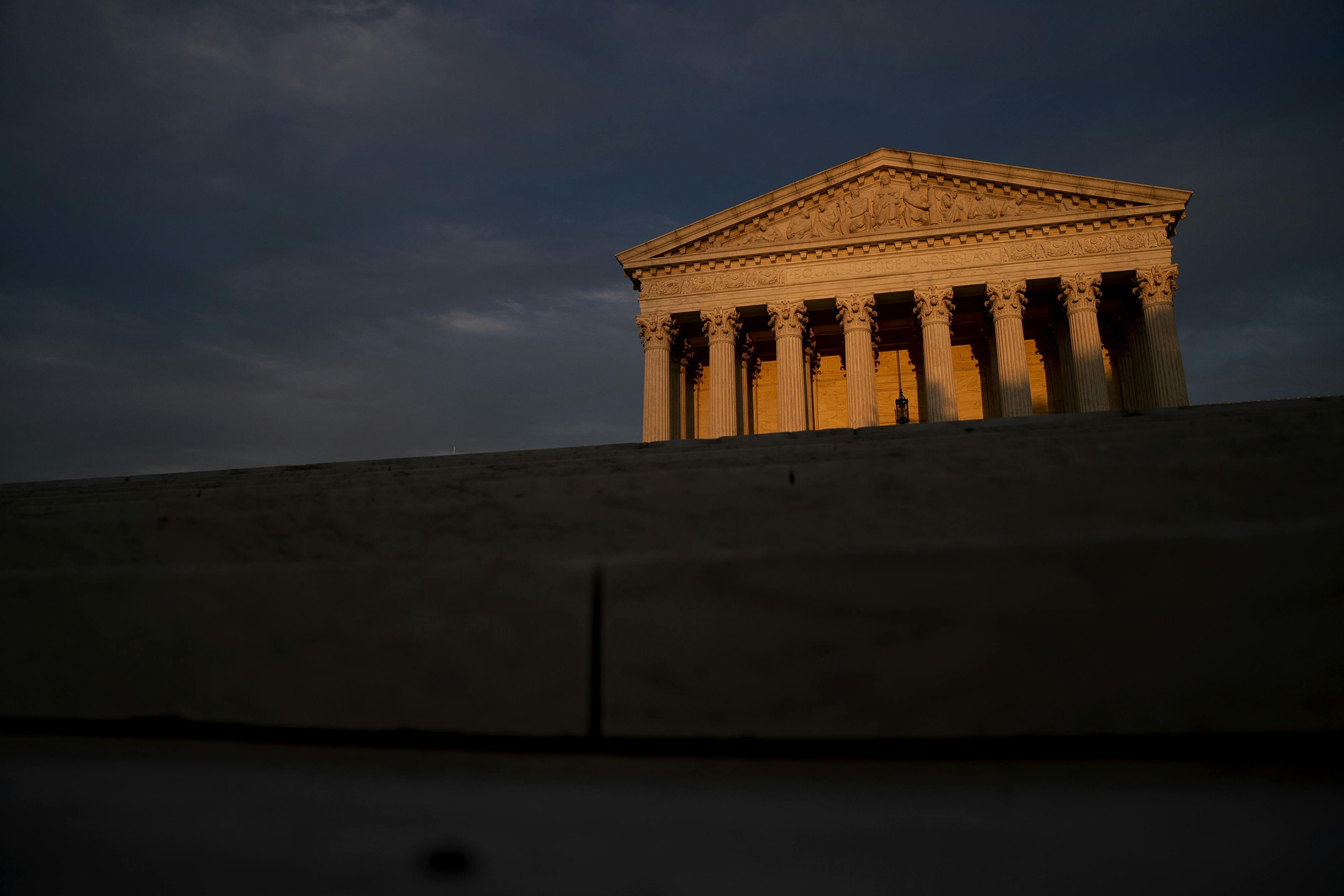The facade of the U.S. Supreme Court lit by a setting sun, foregrounded by shadows.