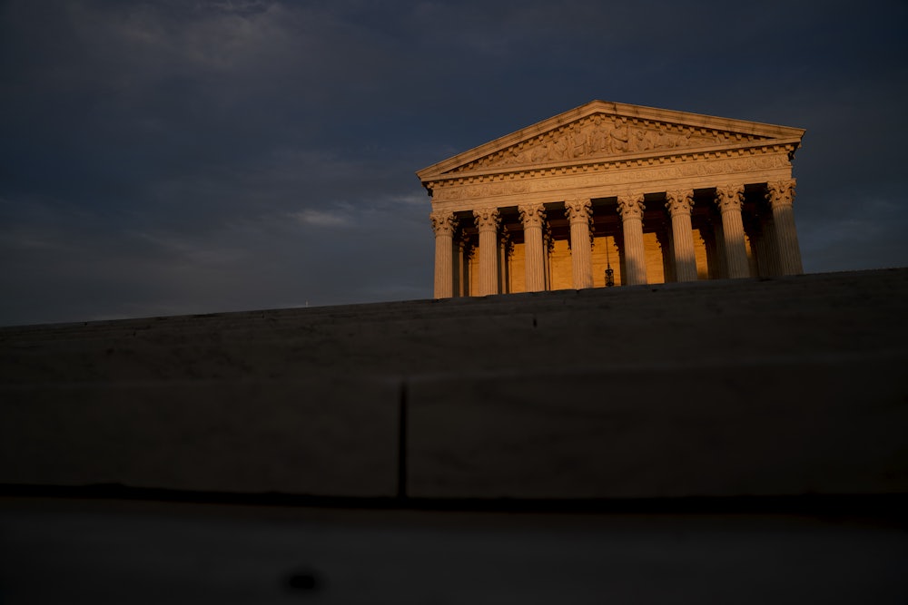 The facade of the U.S. Supreme Court lit by a setting sun, foregrounded by shadows.