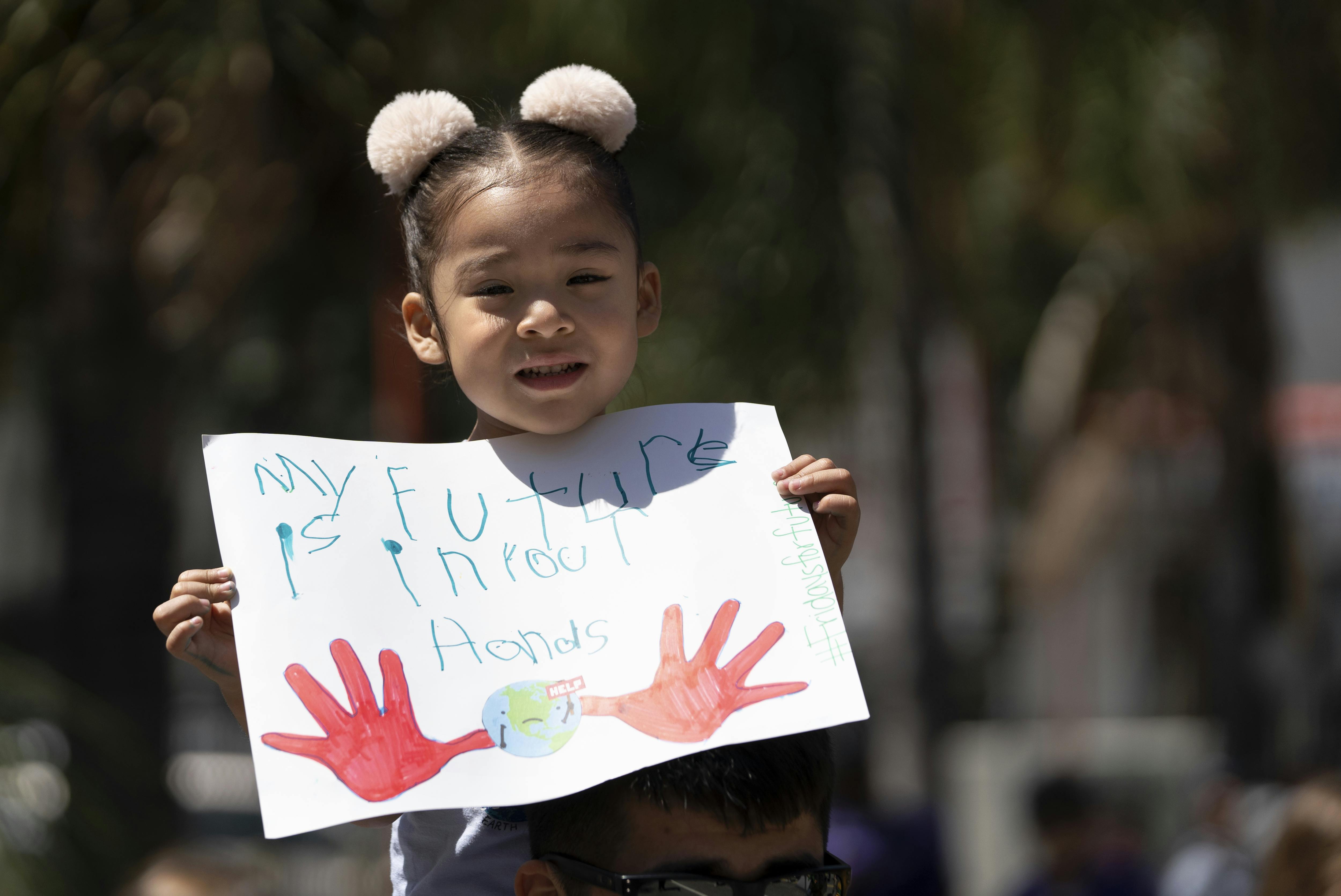 A child holds up a sign saying "my future is in your hands."