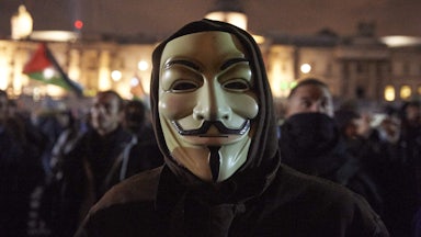 Man wearing a Guy Fawkes mask in the street at nighttime at the “Million Masks March,” organized by the group Anonymous, in London on November 5, 2017