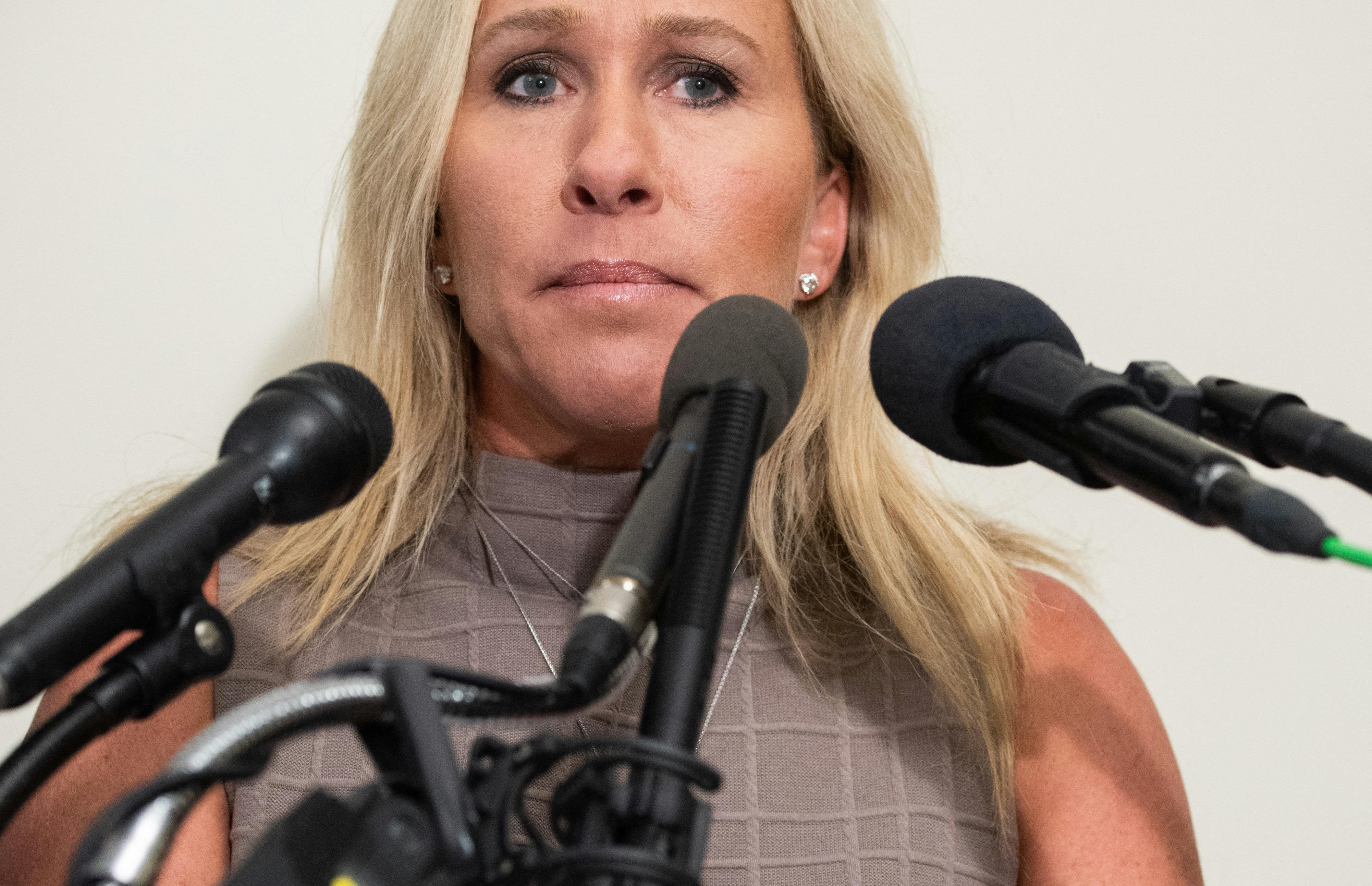 A close up of Marjorie Taylor Greene, surrounded by microphones.