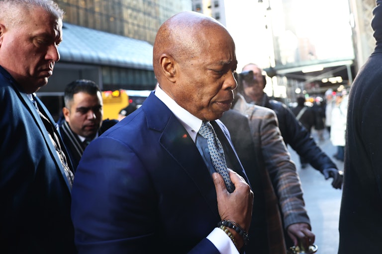 New York City Mayor Eric Adams puts his hand on his tie as he walks, head facing down.