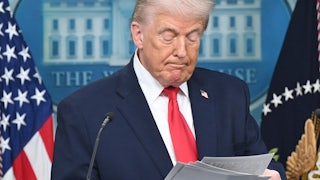 Donald Trump looks down at a stack of paper he's holding while standing at the podium in the White House press briefing room