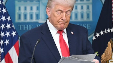 Donald Trump looks down at a stack of paper he's holding while standing at the podium in the White House press briefing room