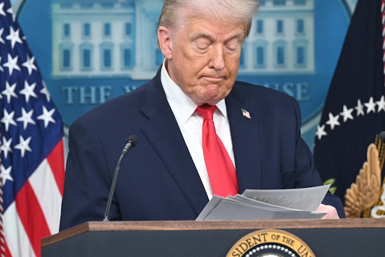 Donald Trump looks down at a stack of paper he's holding while standing at the podium in the White House press briefing room