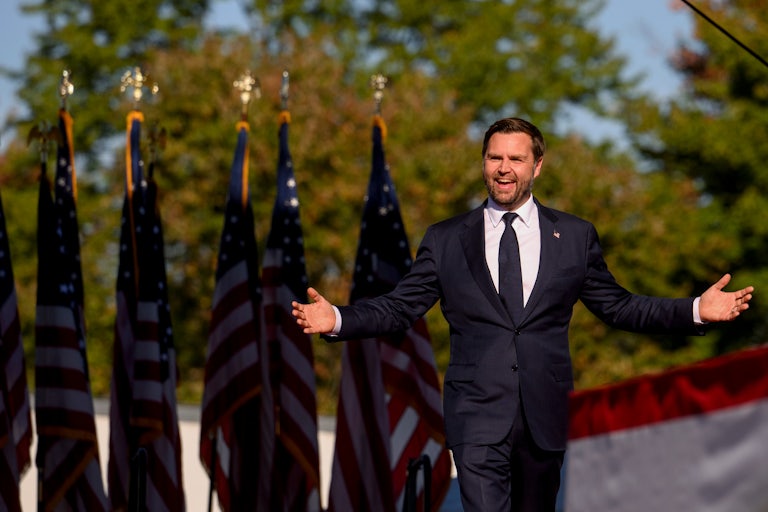 JD Vance smiles and holds his arms out as he walks at a Donald Trump campaign event