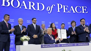 President Donald Trump holds up his signature on the founding charter during a signing ceremony for the “Board of Peace” at the World Economic Forum. He sits at a table as other world leaders stand behind him.