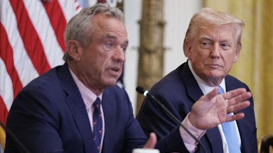 Robert F. Kennedy Jr. sits next to Donald Trump and speaks into microphone while gesturing