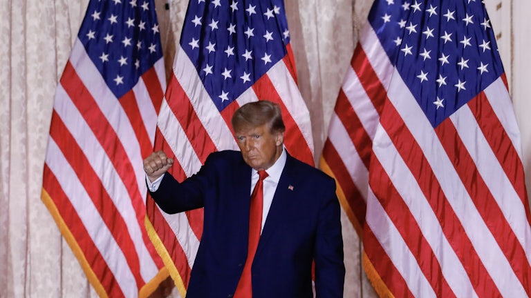 Donald Trump raising a fist and making a weird face with a bunch of US flags in the background