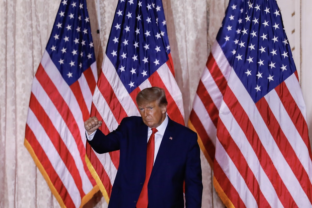 Donald Trump raising a fist and making a weird face with a bunch of US flags in the background