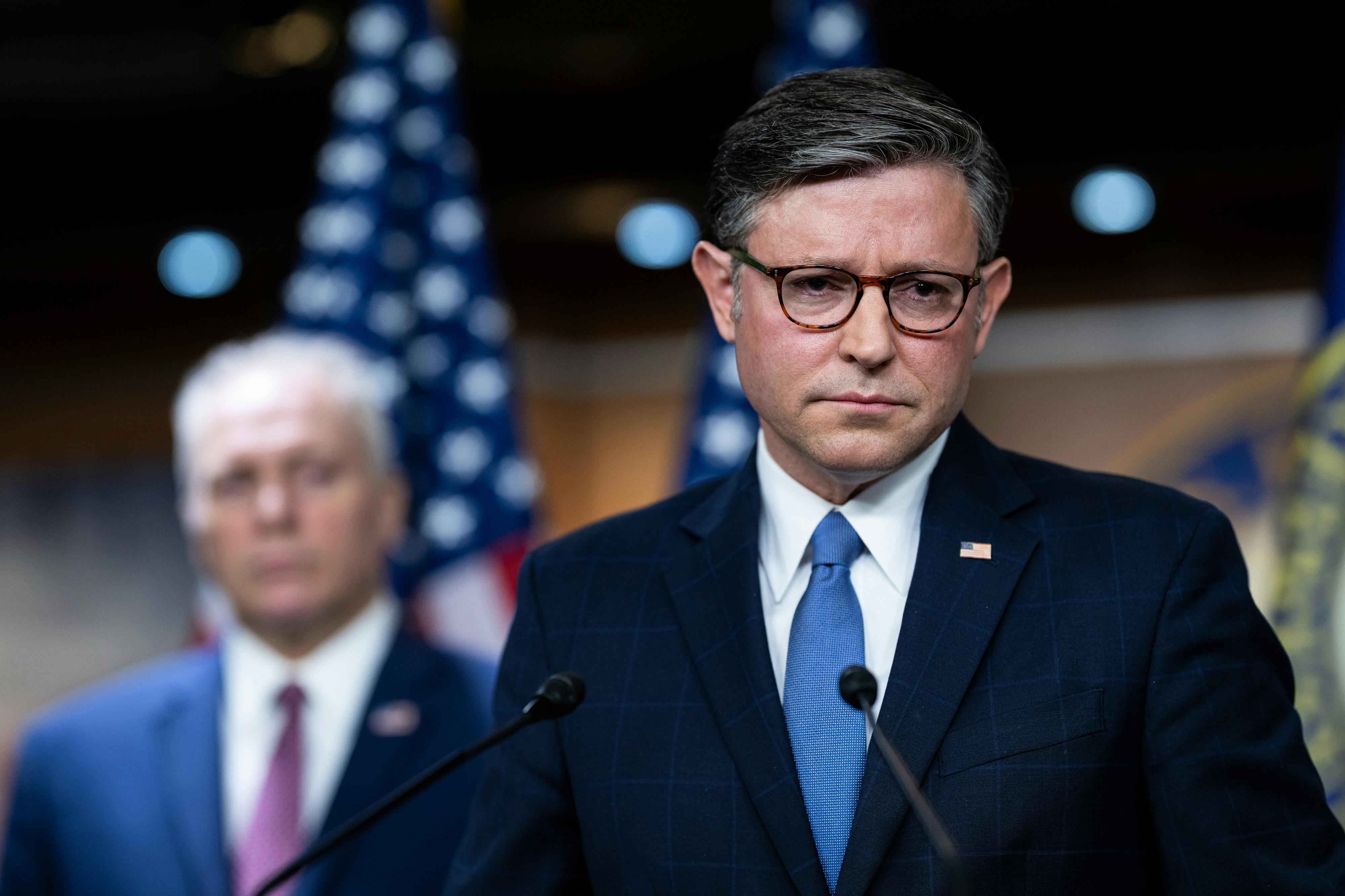 House Speaker Mike Johnson frowns while standing at a podium