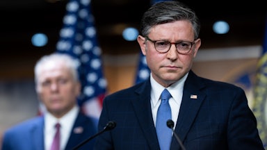 House Speaker Mike Johnson frowns while standing at a podium