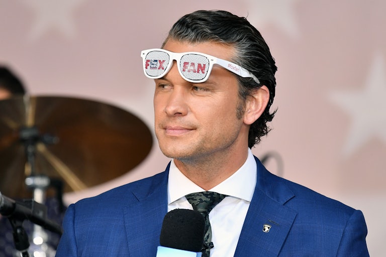 Pete Hegseth holds up a microphone and wears sunglasses that say “Fox Fan”