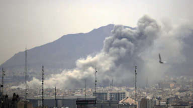 Smoke rises from the Tehran, Iran skyline with the Elborz mountains visible in the background.