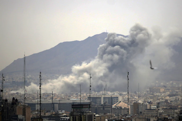 Smoke rises from the Tehran, Iran skyline with the Elborz mountains visible in the background.