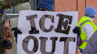 A person holds a sign that says, "ICE out" at a protest