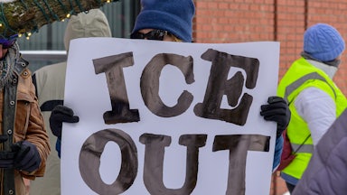 A person holds a sign that says, "ICE out" at a protest