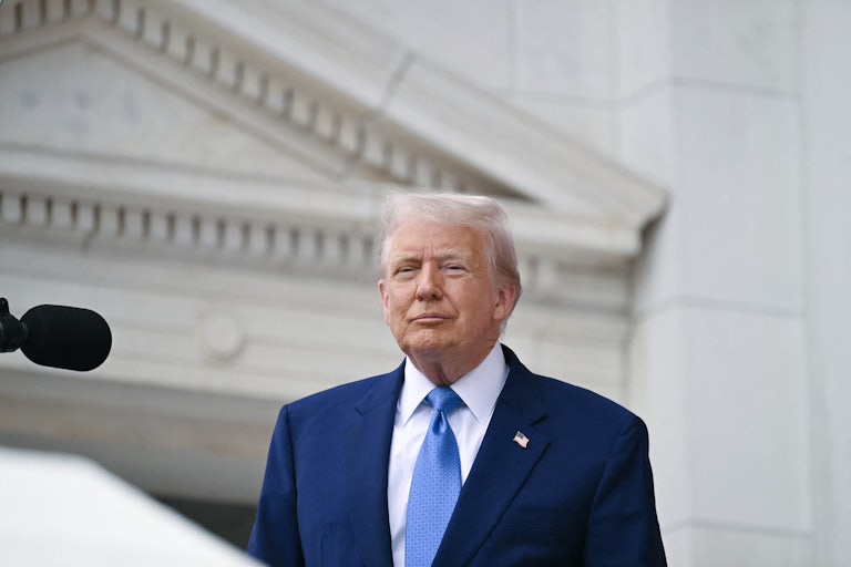 Donald Trump smiles weirdly as he stands in front of a mic.