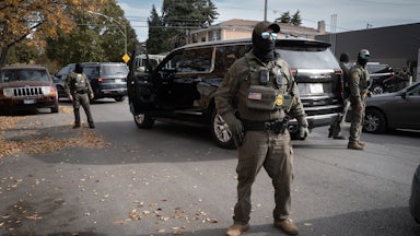 Masked federal agents stand in the street.