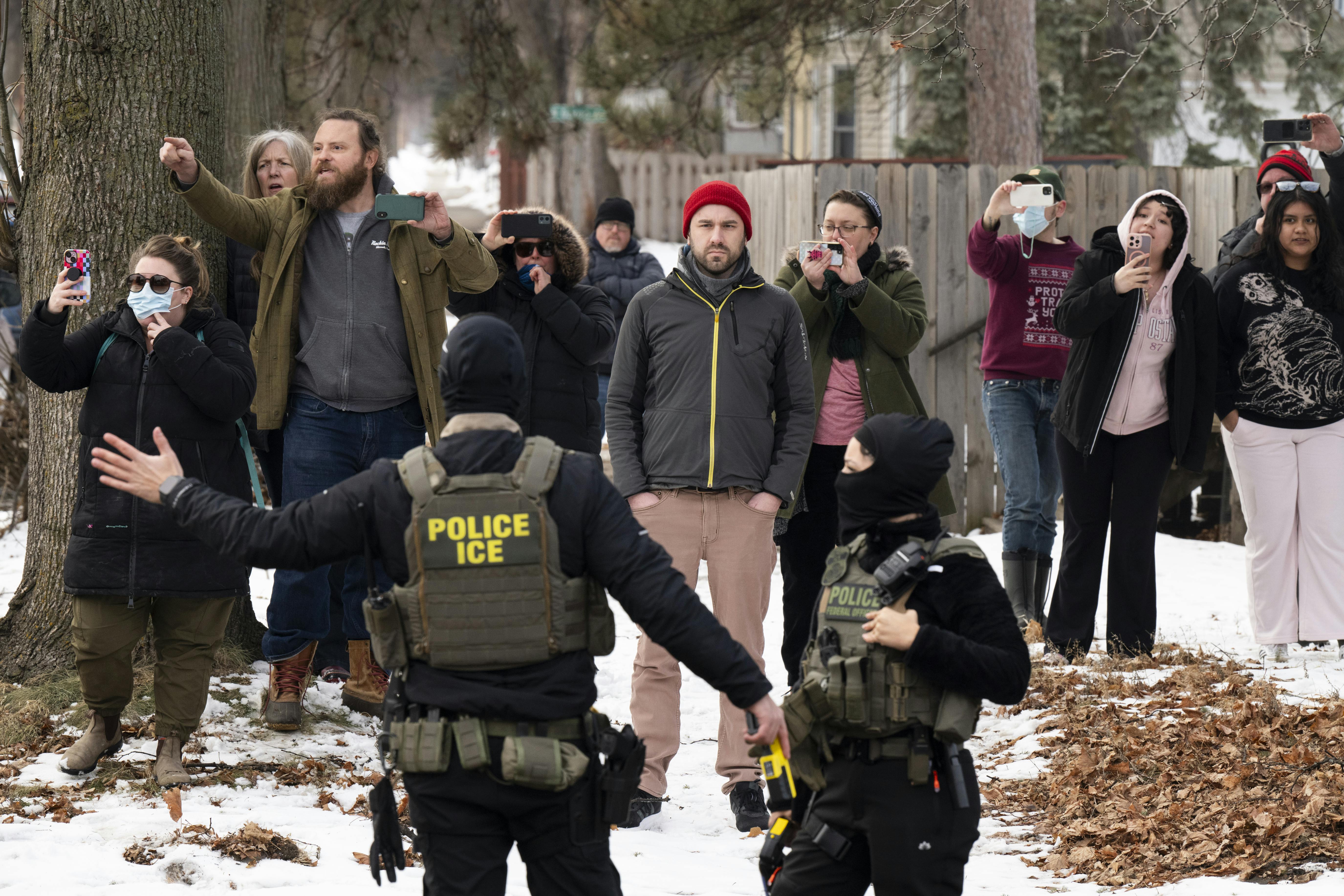 Observers watch and film masked ICE agents in the sidewalk.