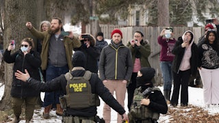 Observers watch and film masked ICE agents in the sidewalk.