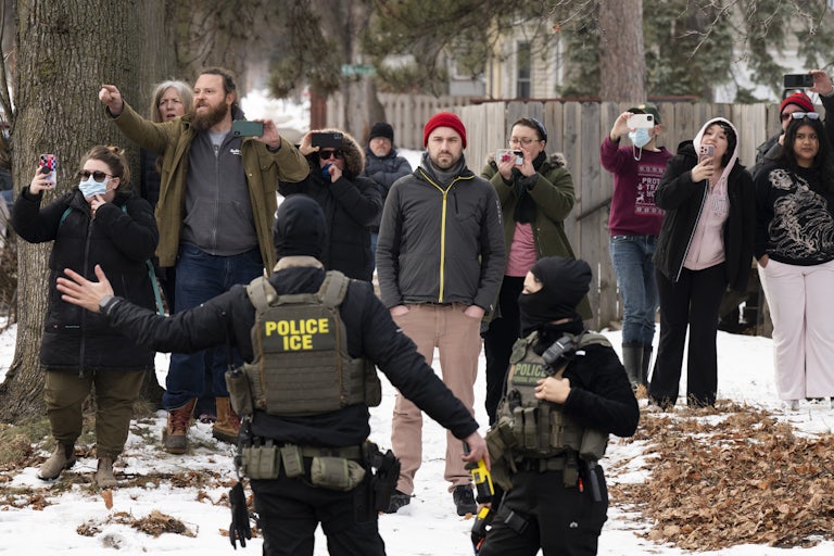 Observers watch and film masked ICE agents in the sidewalk.