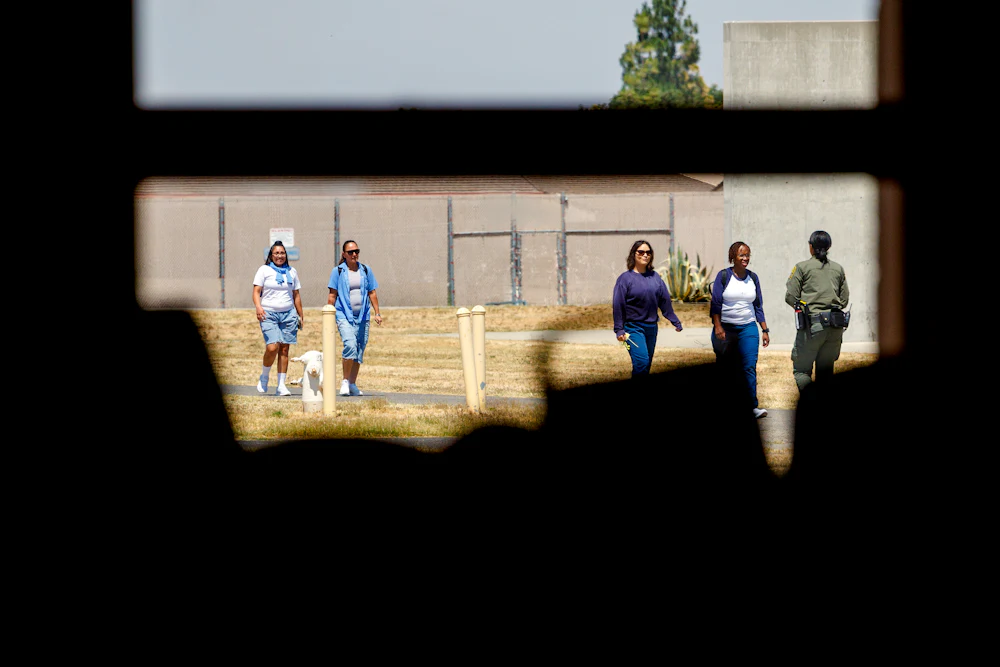 Shone through a window with bars, a guard and women prisoners walk the grounds of the Central California Women’s Facility in Chowchilla, California.