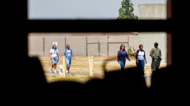 Shone through a window with bars, a guard and women prisoners walk the grounds of the Central California Women’s Facility in Chowchilla, California.