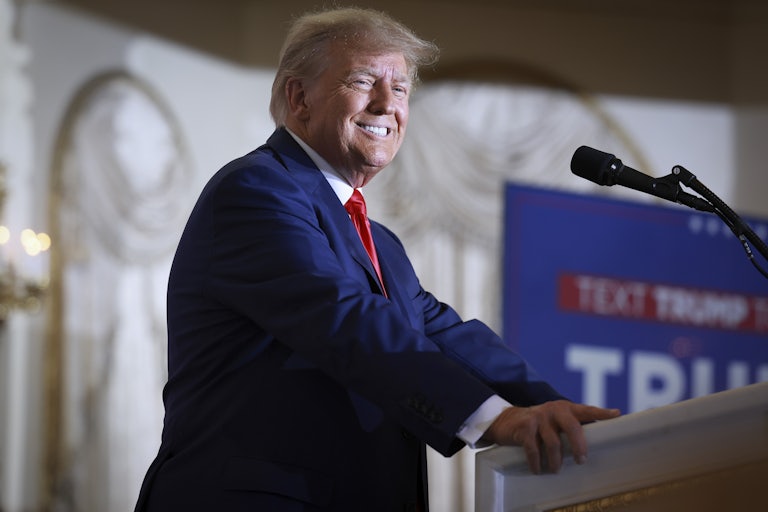 Donald Trump puts his hand on a podium and smiles widely
