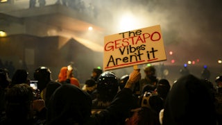 A protester in a crowd holds a sign reading "The Gestapo Vibes Aren't It."