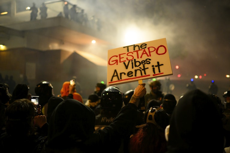 A protester in a crowd holds a sign reading "The Gestapo Vibes Aren't It."