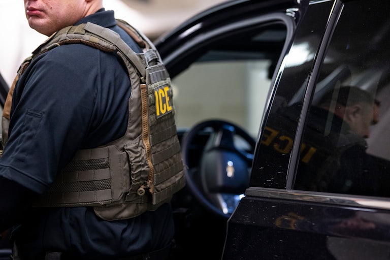 An ICE officer stands next to a car