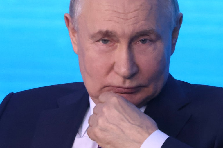 Russian President Vladimir Putin touches his chin while sitting onstage at an event