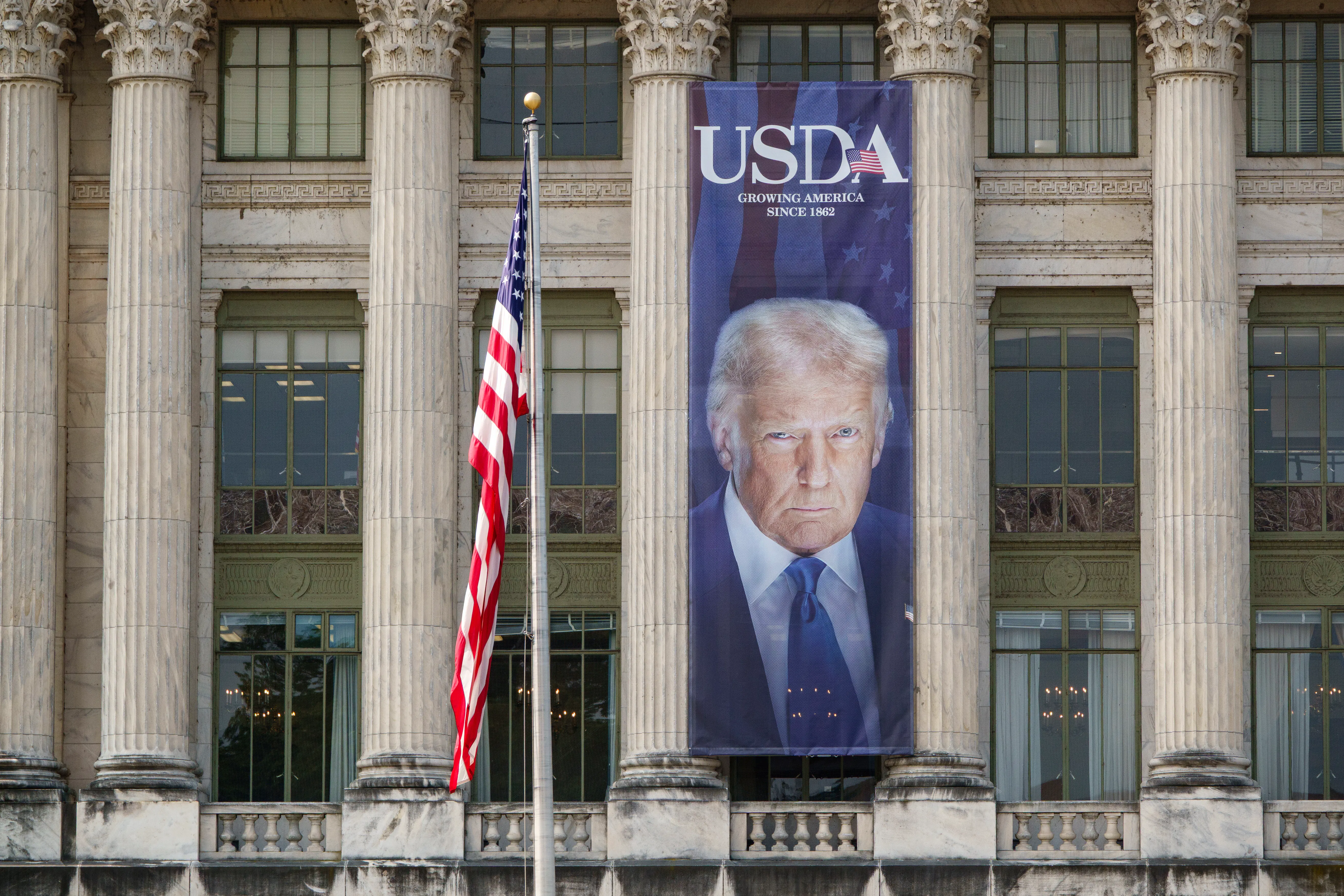 A large banner showing a picture of President Donald Trump on the U.S. Department of Agriculture. The sign reads "USDA Growing America Since 1862."