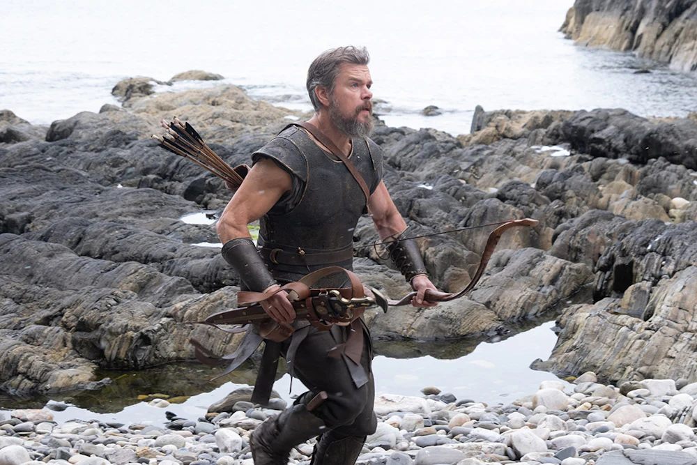 Matt Damon as Odysseus walking over a rocky shoreline in Christopher Nolan’s “The Odyssey”