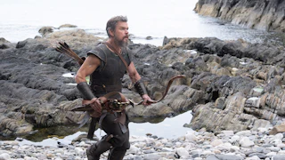 Matt Damon as Odysseus walking over a rocky shoreline in Christopher Nolan’s “The Odyssey”