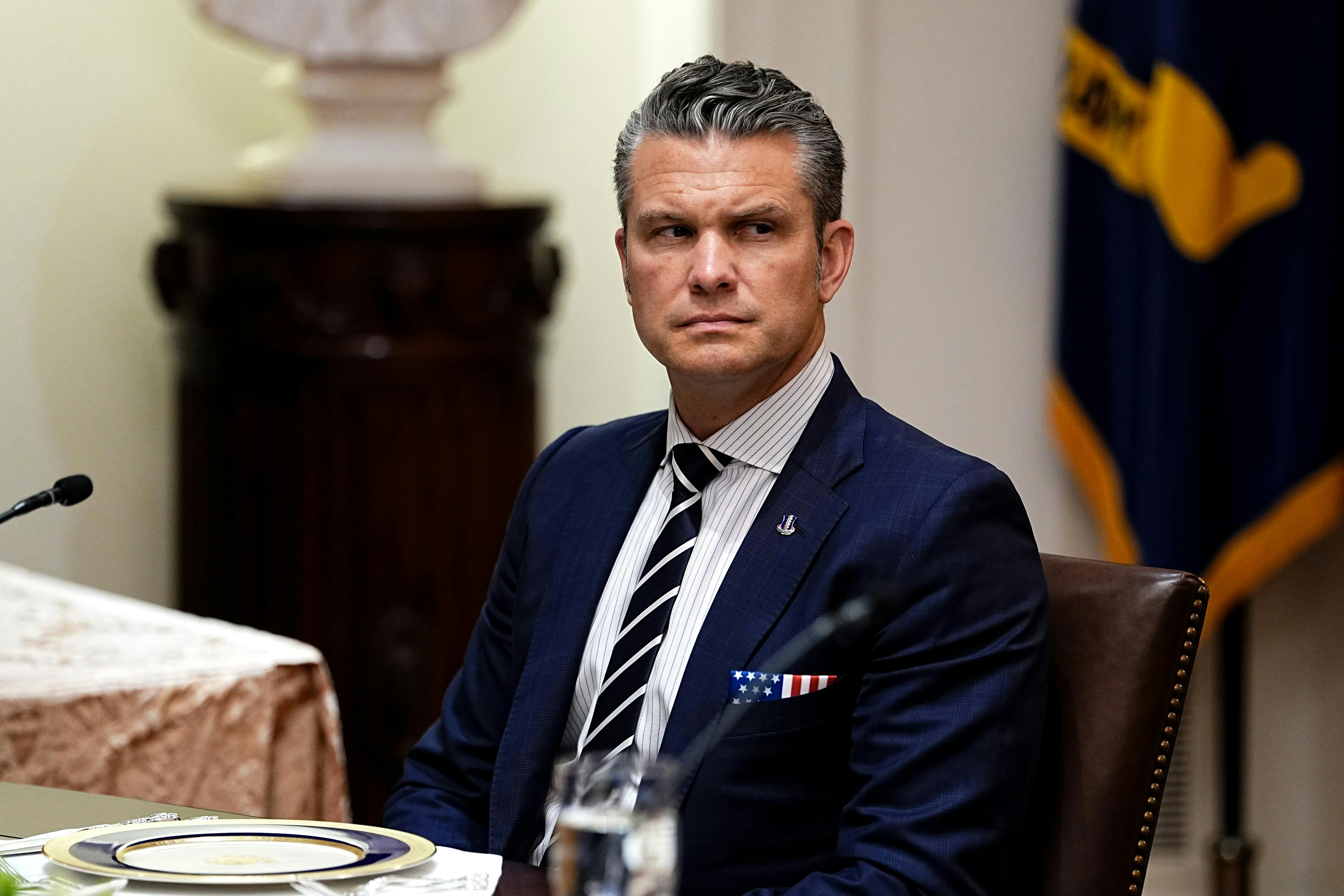 Defense Secretary Pete Hegseth sits at a table