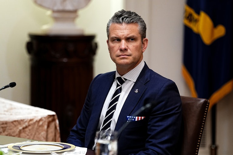 Defense Secretary Pete Hegseth sits at a table