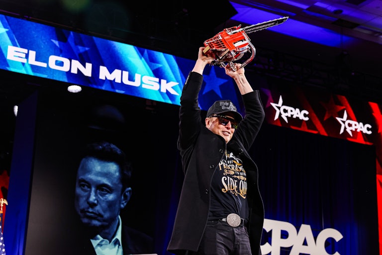 Elon Musk holds a chainsaw above his head while onstage at CPAC