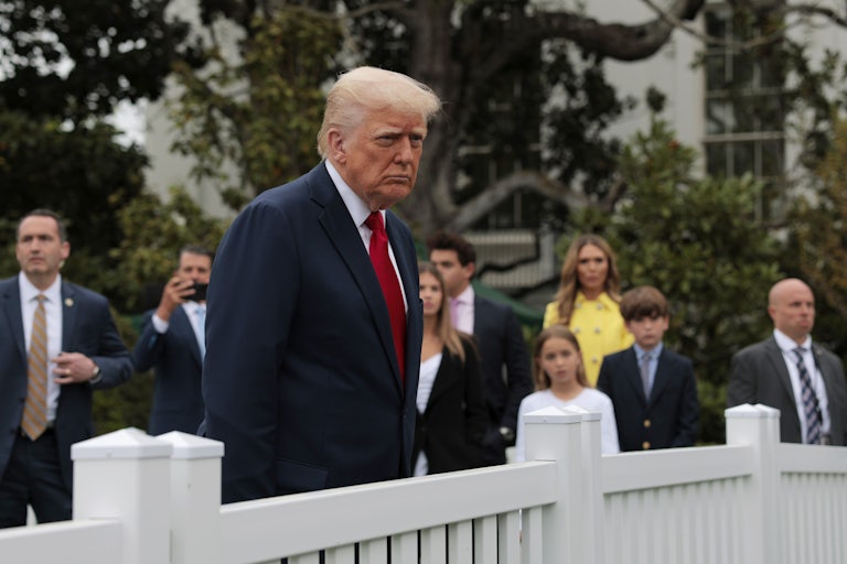 Donald Trump stands behind a fence at the White House Easter Egg Roll. Others are in the background.