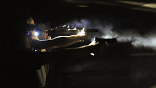 A line of men perform a nighttime gun drill.