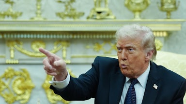 Donald Trump puckers his lips and points while sitting in the Oval Office