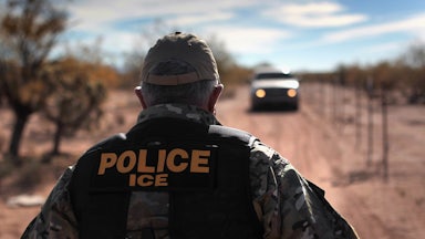 An ICE agent faces away from the camera